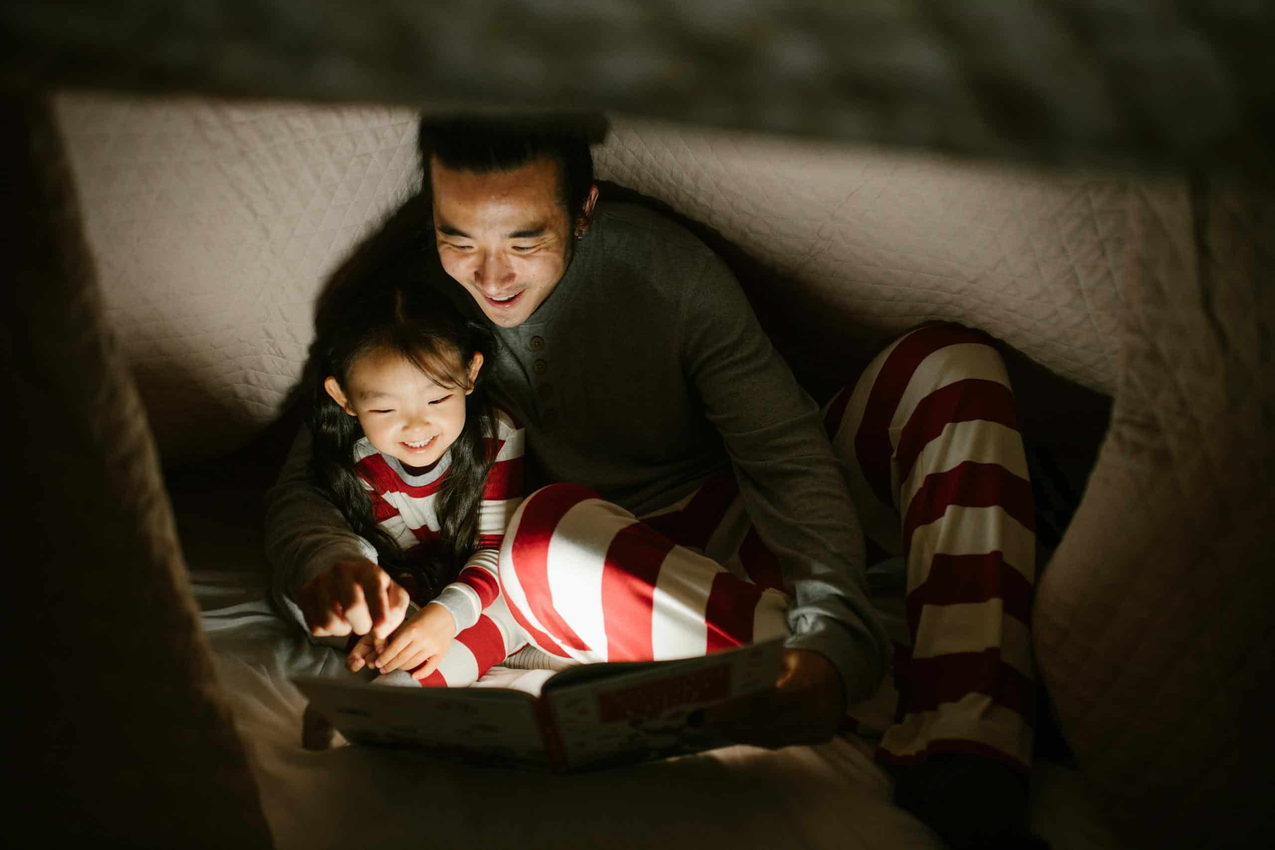 Father with Daughter Reading Book under Blanket